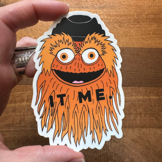 A hand holding a Philly-themed vinyl sticker of a whimsical orange character with the word 