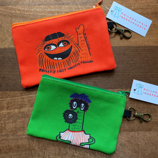 Two colorful Gritty & Phanatic zipper pouches with cartoon characters embroidered on them, lying on a wooden surface. Brand Name: Ana Thorne