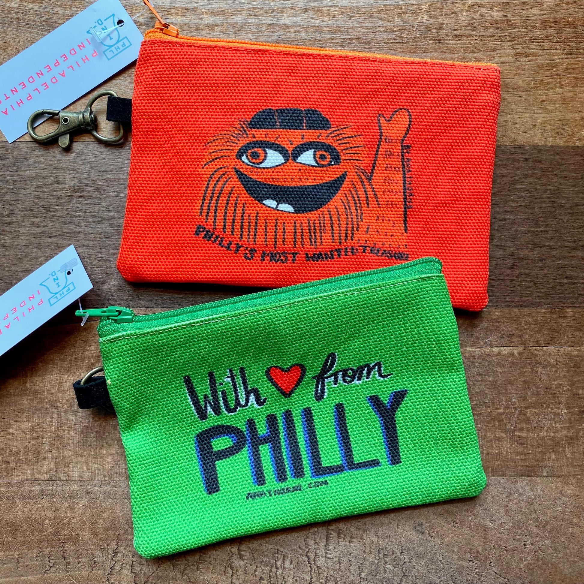 Two colorful Ana Thorne Gritty & Phanatic zipper pouches with "with ♥️ from Philly" and a stylized illustration on a wooden background.