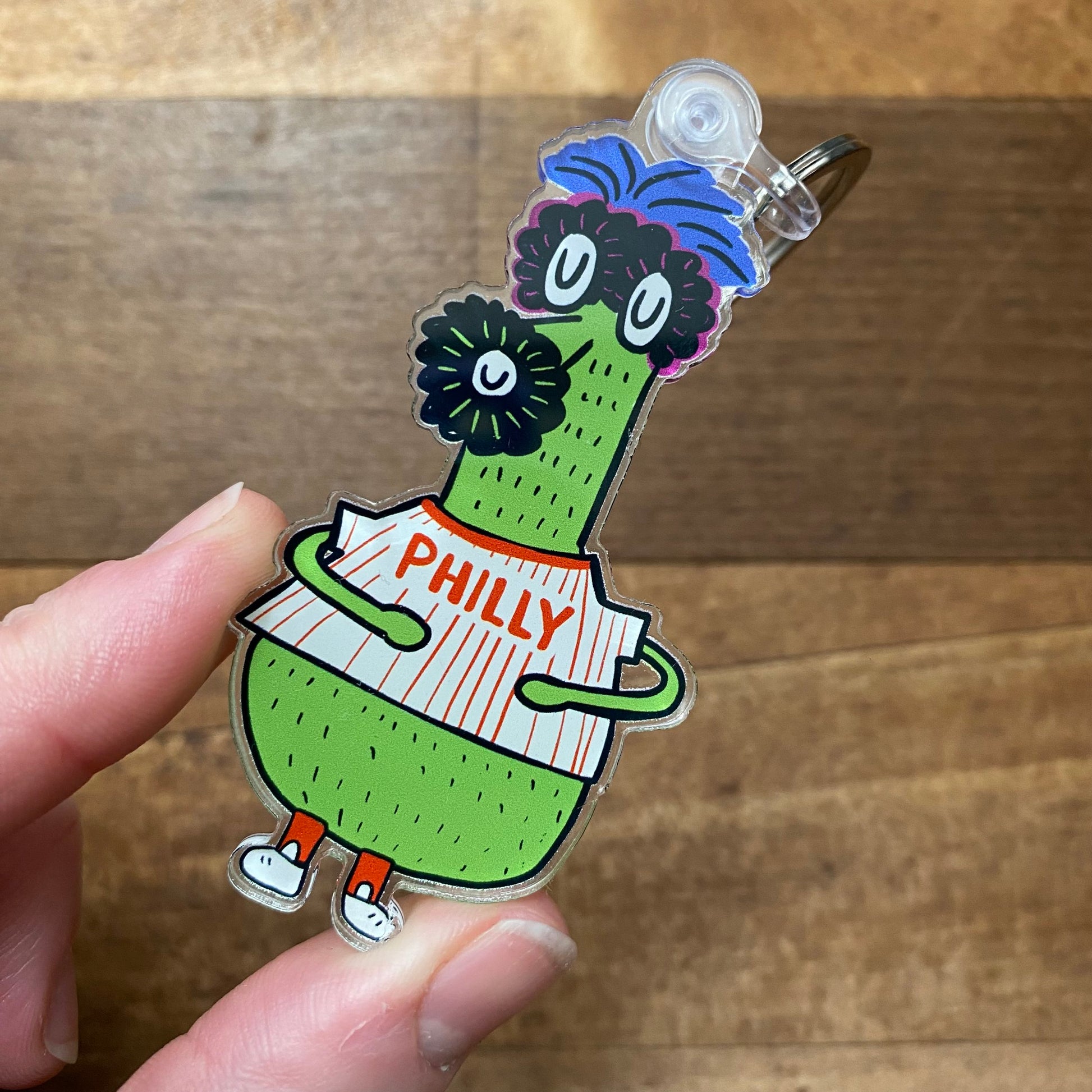 A hand holds an Ana Thorne Gritty & Phanatic Keychain featuring a cartoonish green character with glasses, a blue topknot, and a white "Philly" shirt.