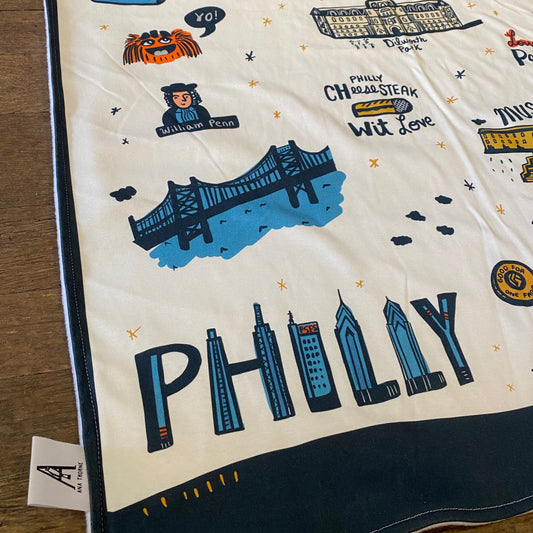 A decorative PHL Icons Baby Blanket featuring illustrations and text related to Philadelphia, including the Liberty Bell, a cheesesteak sandwich, and city landmarks by Ana Thorne.