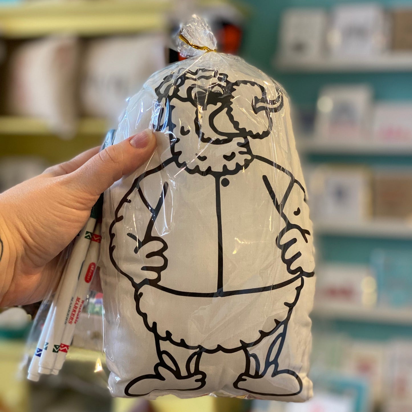 A hand holding a packaged plush toy of the Phanatic, with its characteristic round belly and quirky appearance, in a store by Doodle Jawnz Washable Kits.