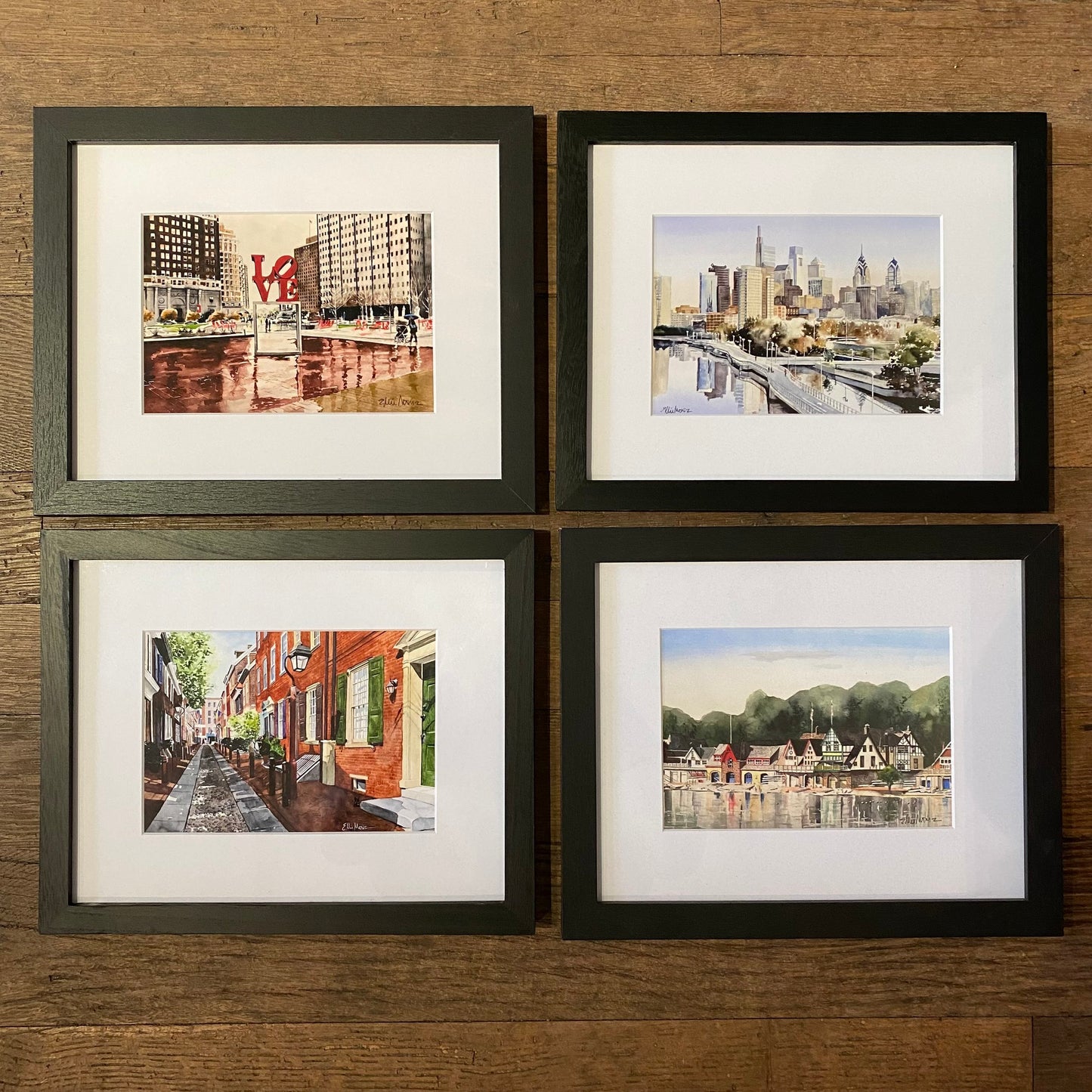 A group of Ellie Moniz Framed Philly Watercolor Prints on a wood surface.