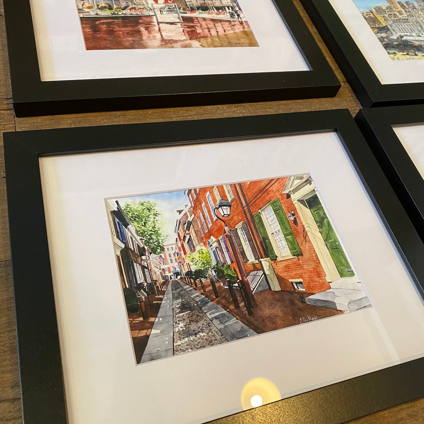 Three Framed Philly Watercolor Prints displayed on a wall, showcasing vibrant urban scenes with Philadelphia architecture and streets by Ellie Moniz.