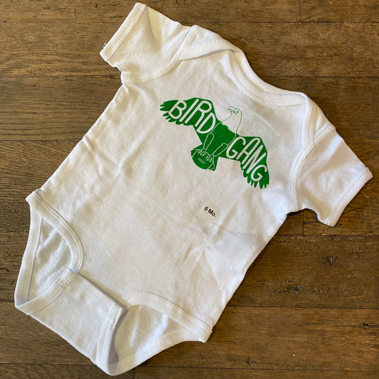 White 100% cotton exit343design Bird Gang Baby Onesie with "bird gang" and a hanger graphic printed on it, displayed on a wooden surface.