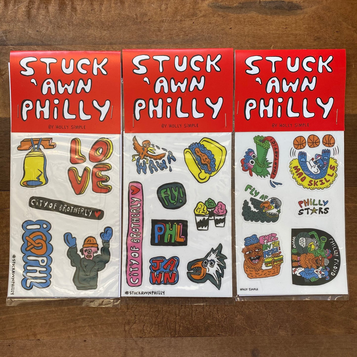 Collection of vibrant Holly Simple Philly Sticker Packs, including Rocky and Wawa designs, displayed on a wooden surface.