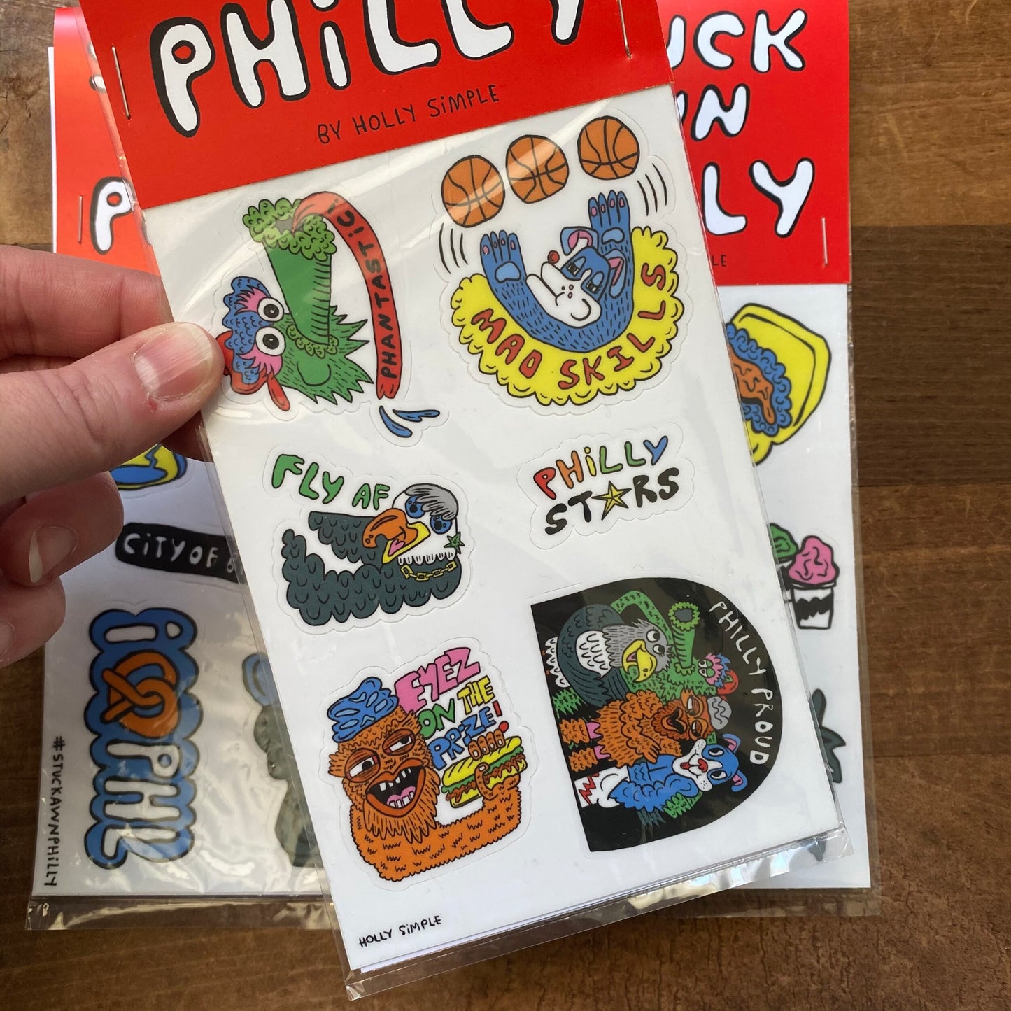 A person holding a package of Holly Simple Philly Sticker Packs featuring iconic symbols, sports references, and Rocky.