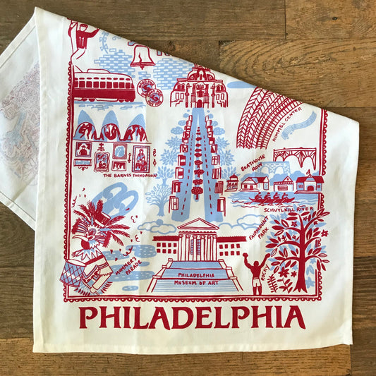 A decorative Philadelphia Tea Towel by Jean Mason, featuring iconic landmarks and symbols of the city, perfect as a host gift.