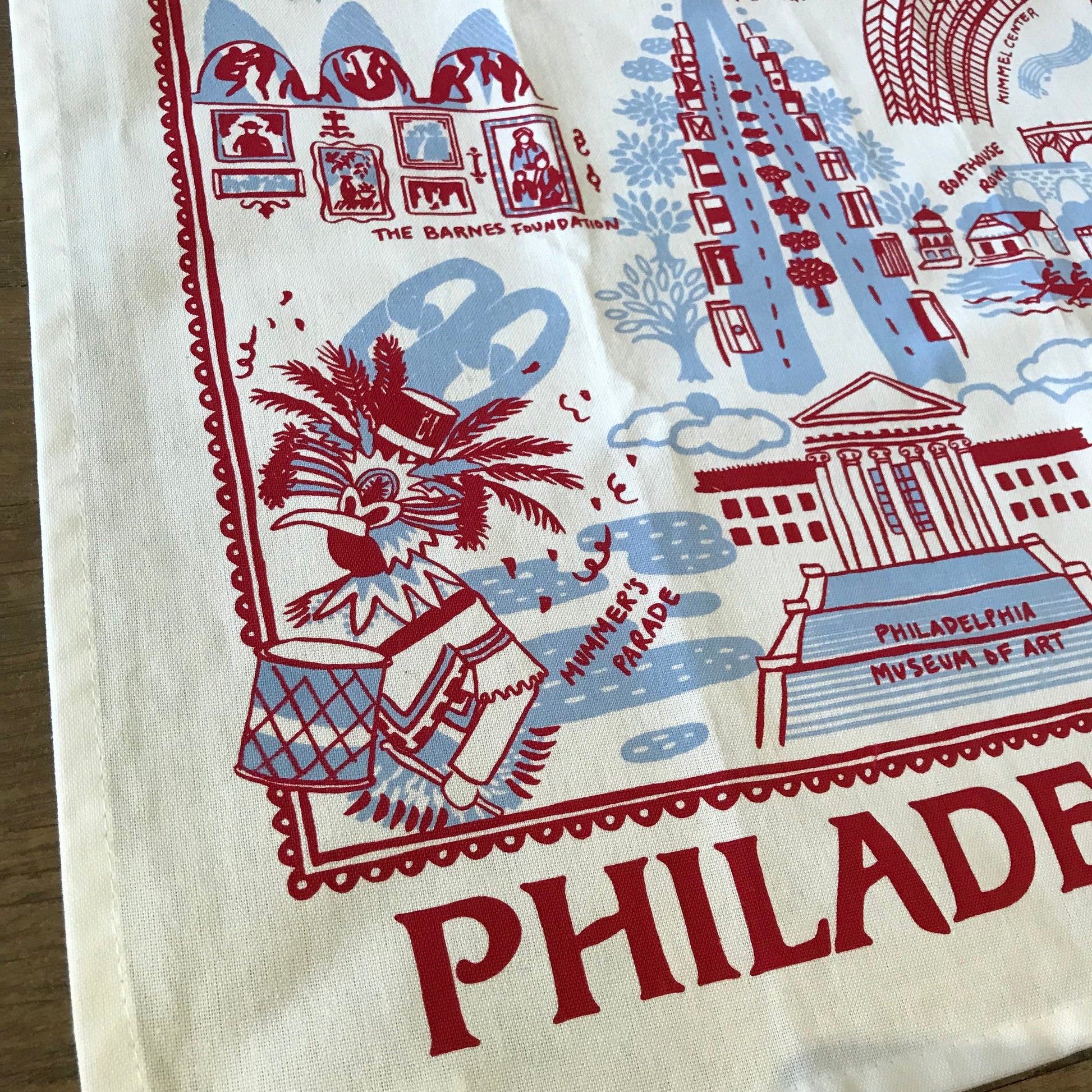 A souvenir Philadelphia Tea Towel with red illustrations and text featuring landmarks and symbols of Philadelphia, perfect as a host gift by Jean Mason.