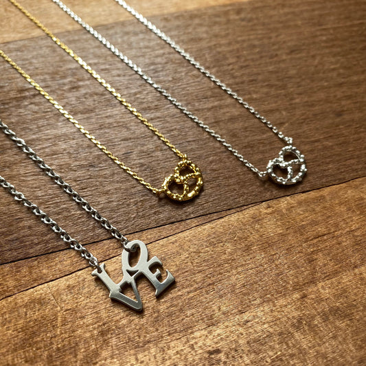 Three LOVE & Pretzel necklaces with different pendant designs, including Philly pride necklaces, laid out on a wooden surface by Lily Lough.