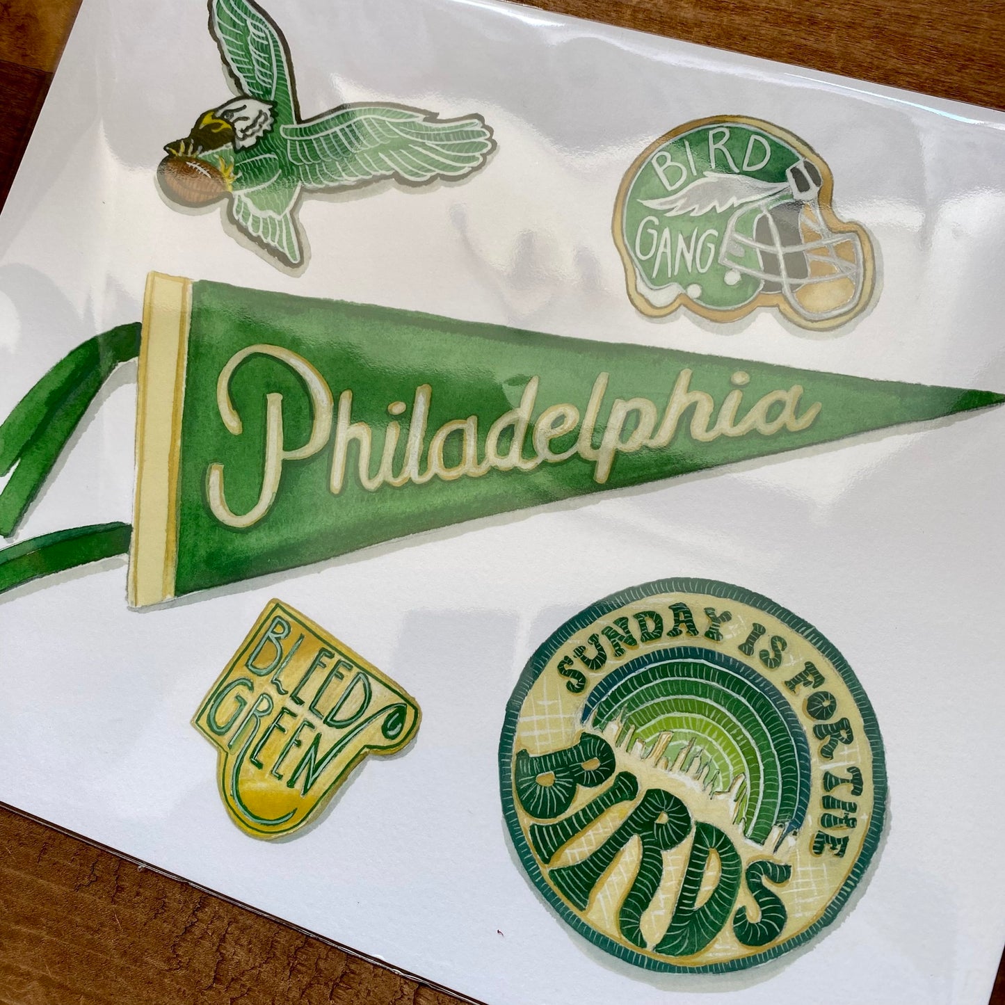 A collection of Meadowbrook Lane's Philly Sports Prints and a pennant displayed on a wooden surface.