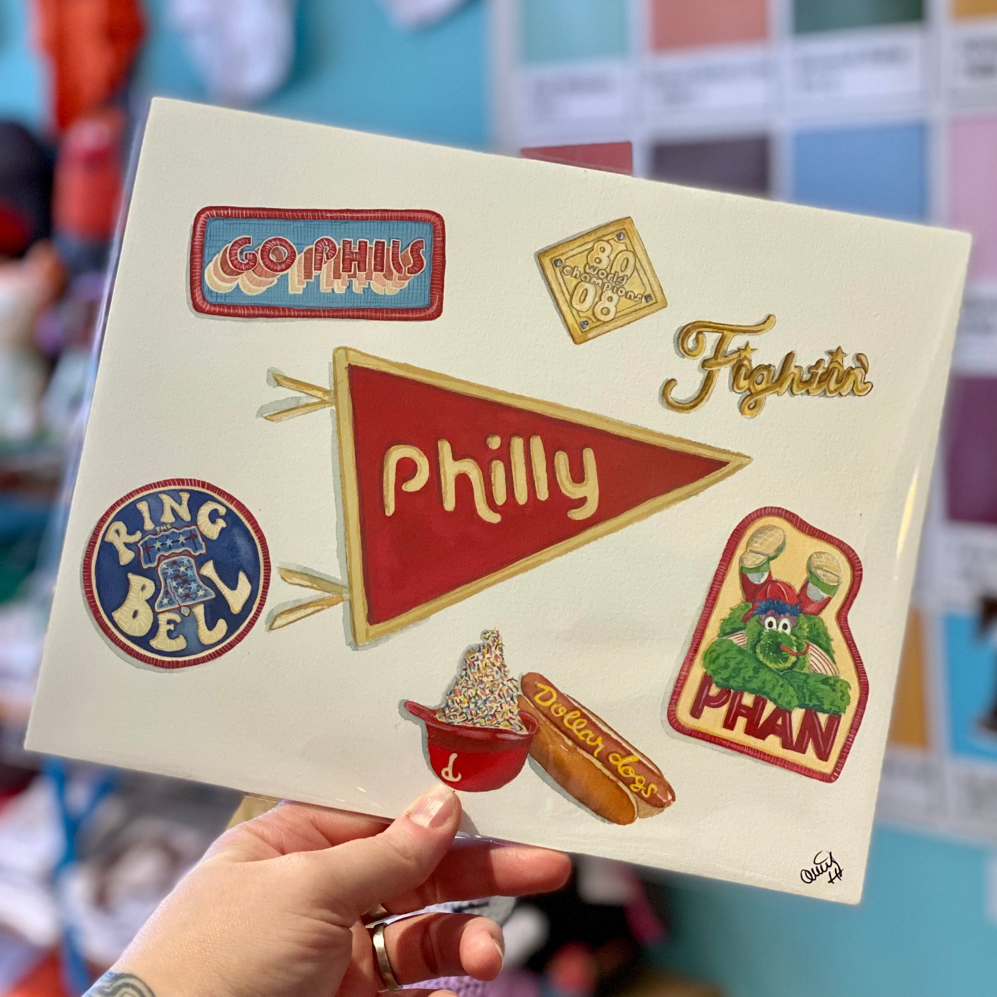 Hand holding a canvas with colorful Philly Sports Prints representing Philadelphia sports teams and icons by Meadowbrook Lane.