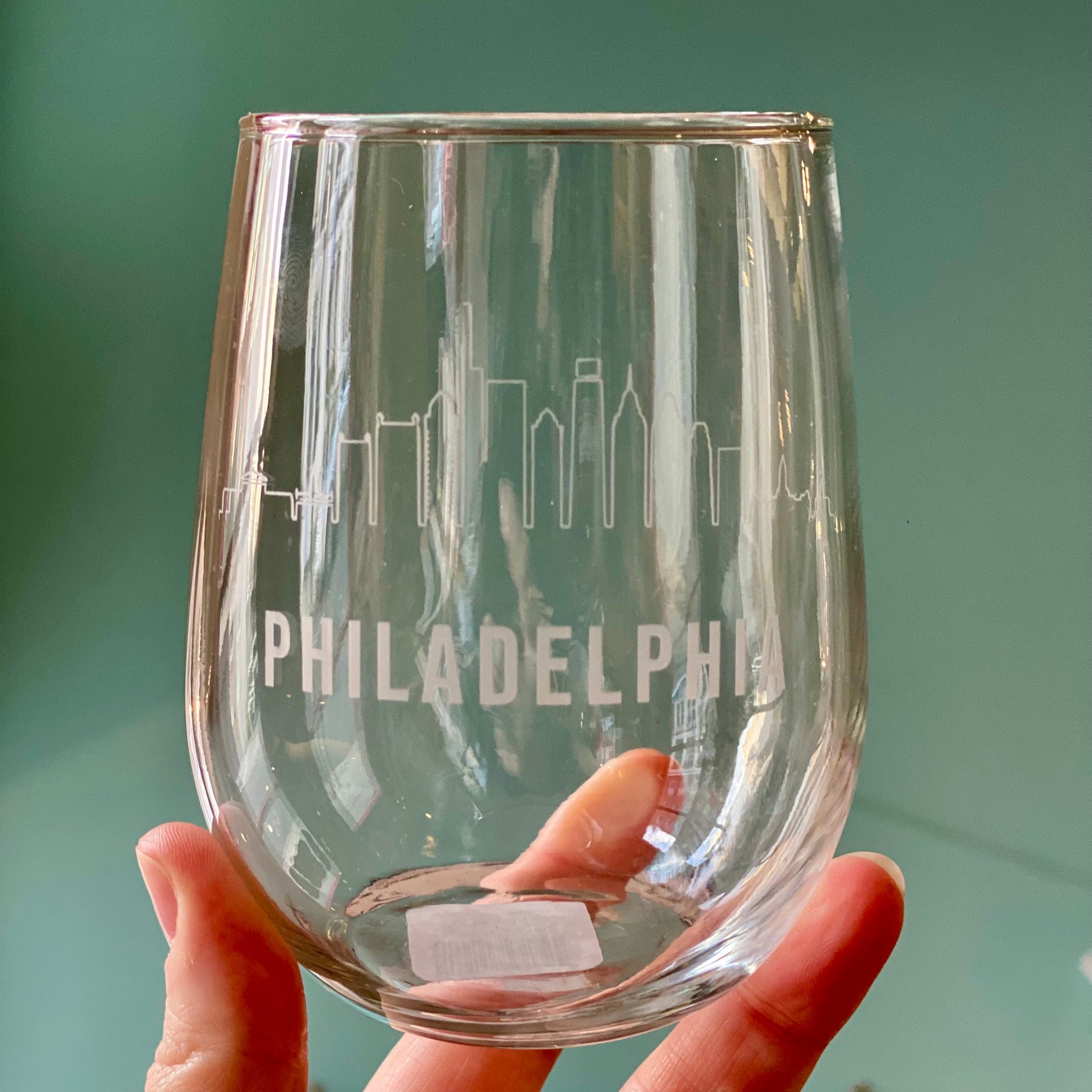 A hand holding a Philly Etched Wine & Rocks Glassware from Morning Fog Studios with the Philadelphia skyline meticulously detailed on it.