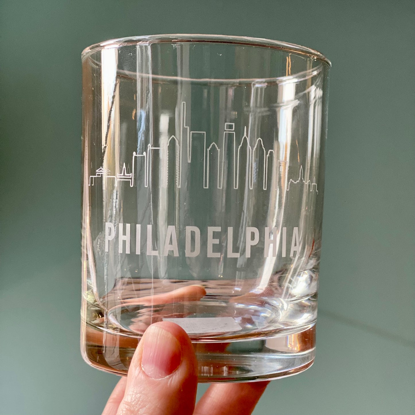 A hand holding a Philly Etched Wine & Rocks Glassware from Morning Fog Studios with an etched skyline of Philadelphia.