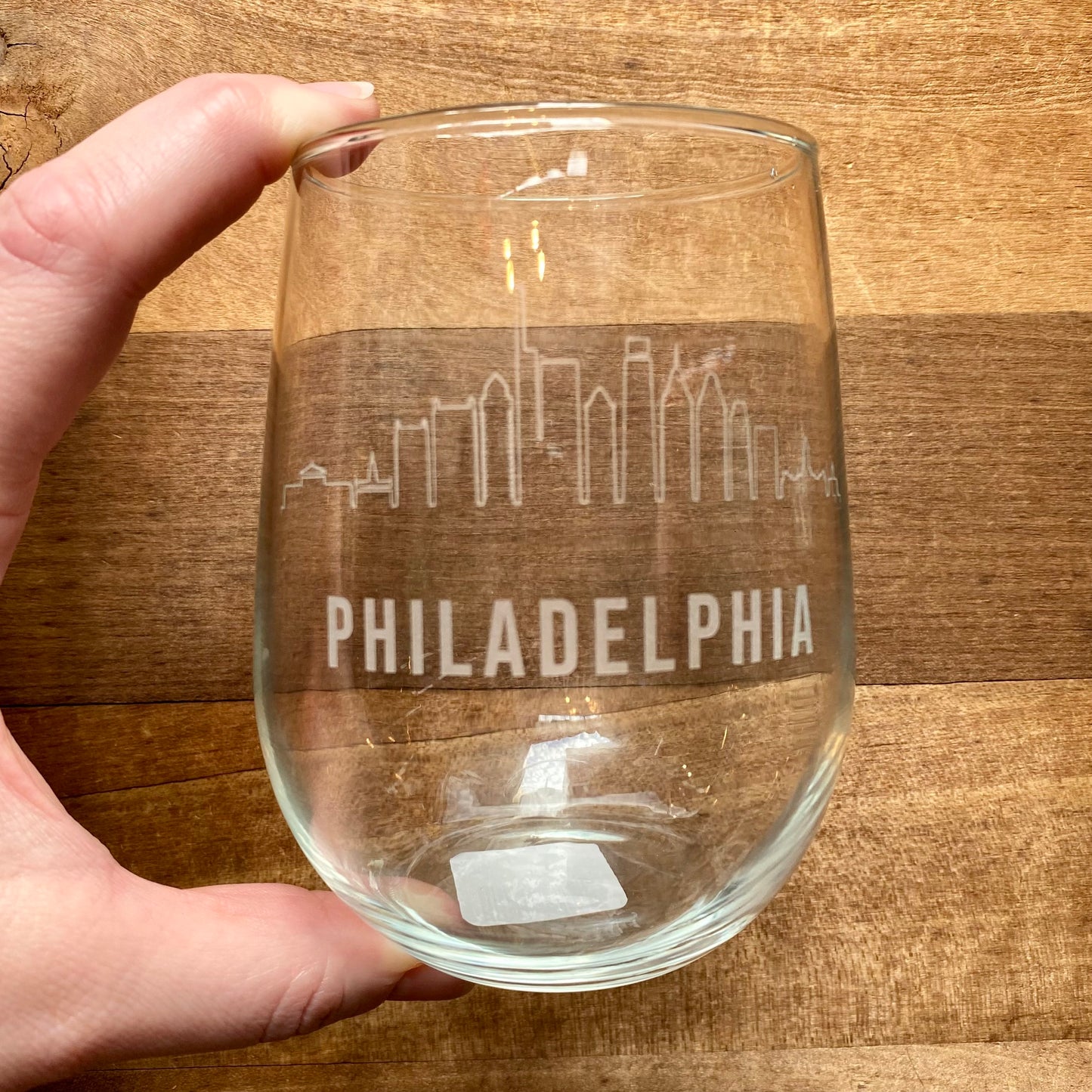 Hand holding a Philly Etched Wine & Rocks Glassware with an etched Philadelphia skyline design from Morning Fog Studios.