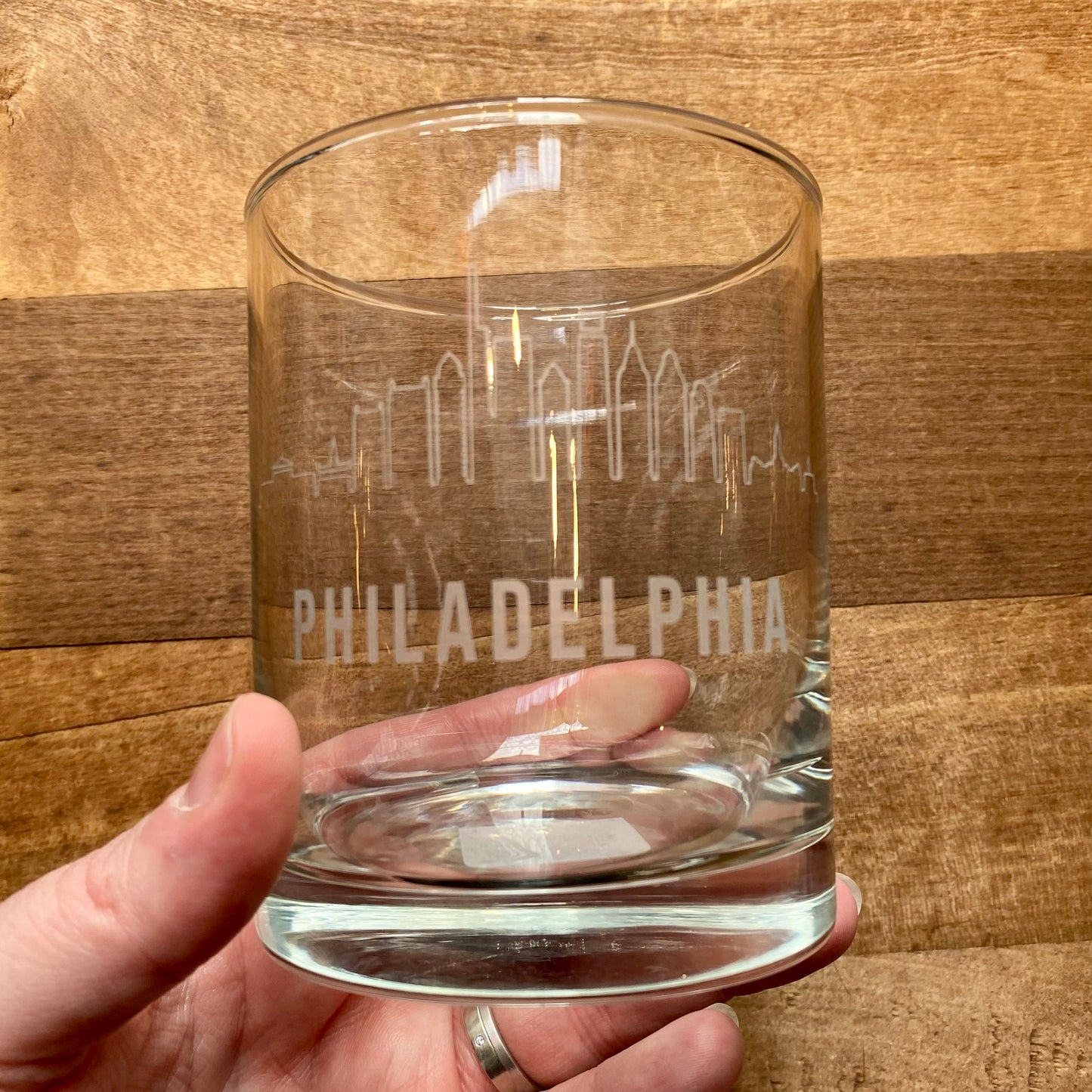 Hand holding a Philly Etched Wine & Rocks Glassware with "Philadelphia" and a skyline design by Morning Fog Studios.