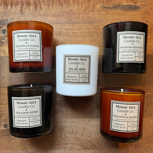 Four soy wax candles from Mount Airy Candle Co., arranged on a wooden surface, featuring different aromatic scents in Glass Tumblers.