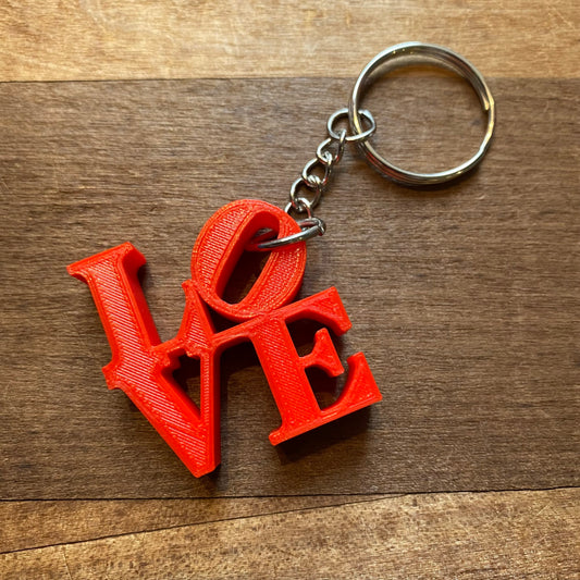 3D printed Rosewood Home LOVE Keychain on a wooden surface.