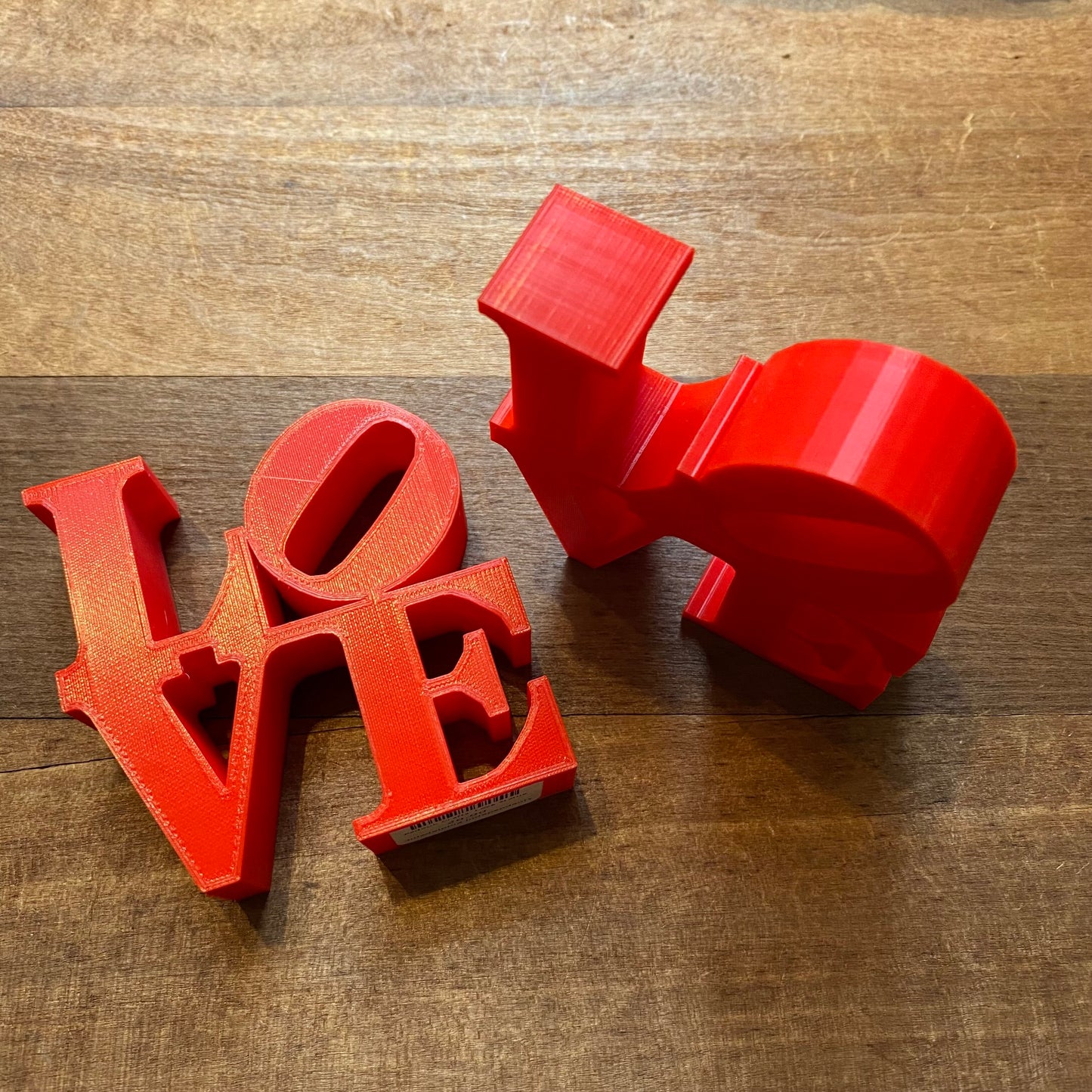 Red Rosewood Home LOVE Statue replicas on a wooden surface.