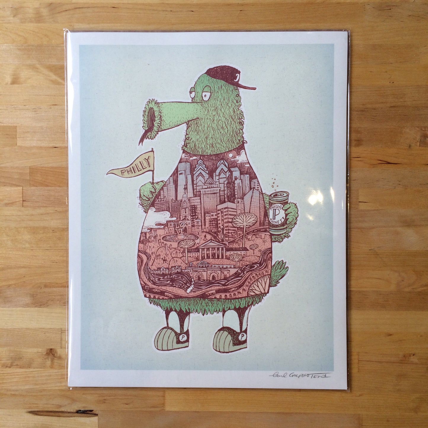 Illustration of a whimsical green creature resembling the Phillies Phanatic, wearing a cap, holding a 'philly' pennant, with a cityscape drawn on its body, framed and displayed as the Paul Carpenter Phanatic Print.