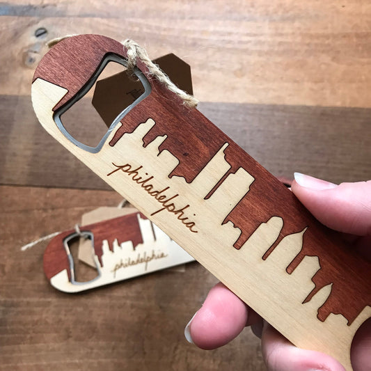 A hand holding a Philly Phlights Philly Bottle Opener with a city skyline design and the word 