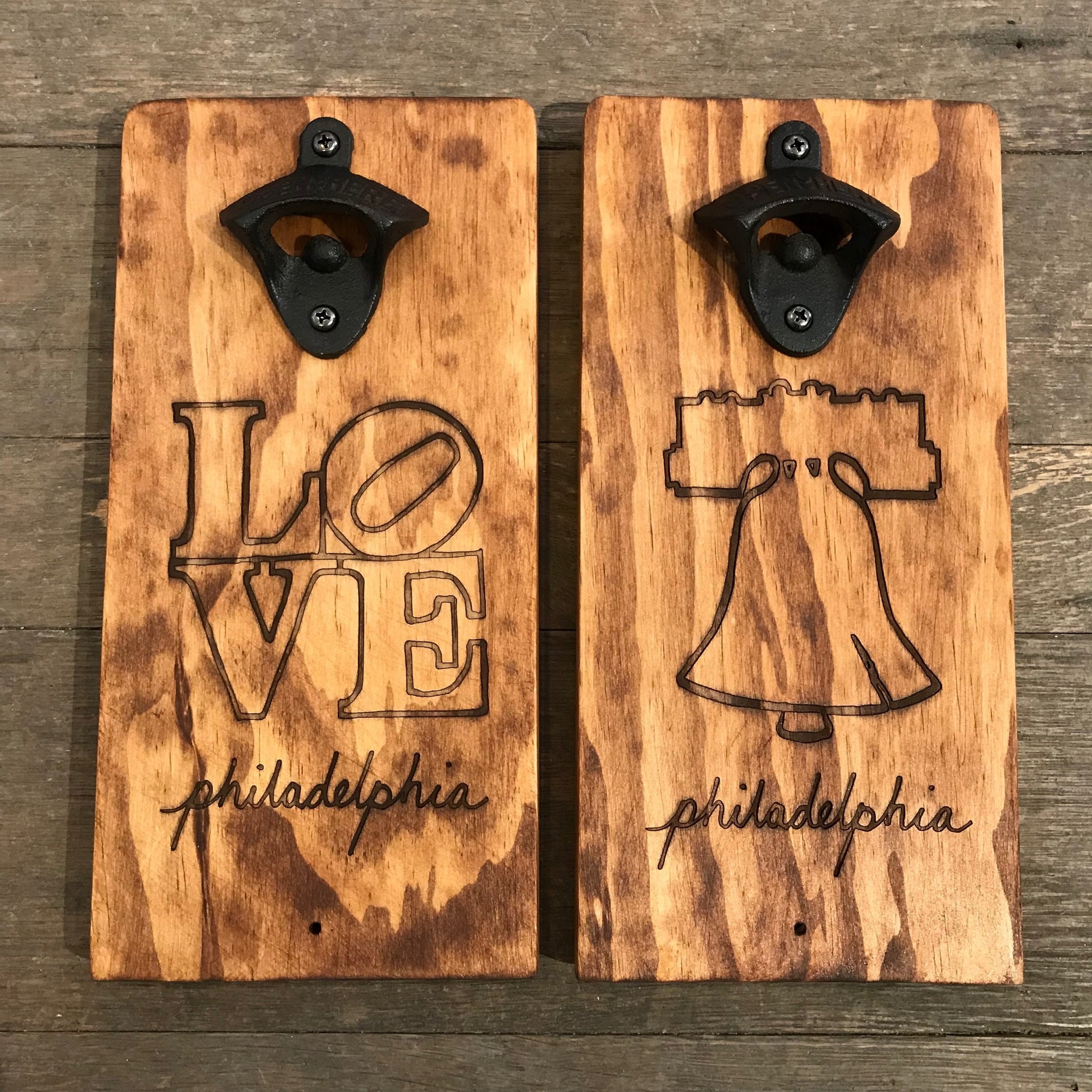 Two Philly Phlights Philly Wall-Mounted Bottle Openers laser-etched with "Love Philadelphia" and the iconic Liberty Bell, mounted on a rustic wood background.