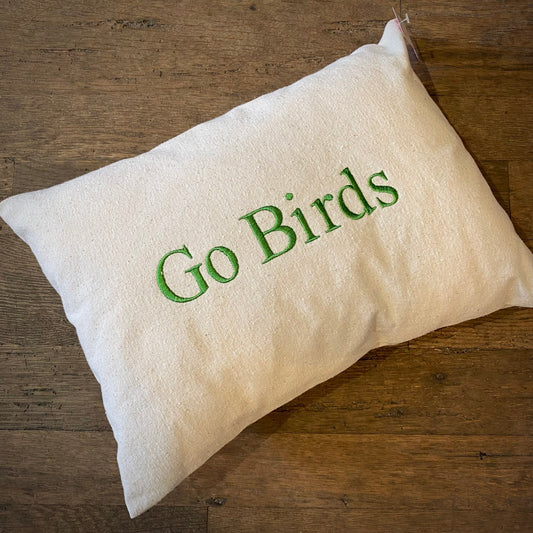 A white Go Birds Embroidered Pillow made from 100% unbleached cotton drill fabric, with the words "go birds" embroidered in kelly green on a wooden surface, by The Pillow Works.