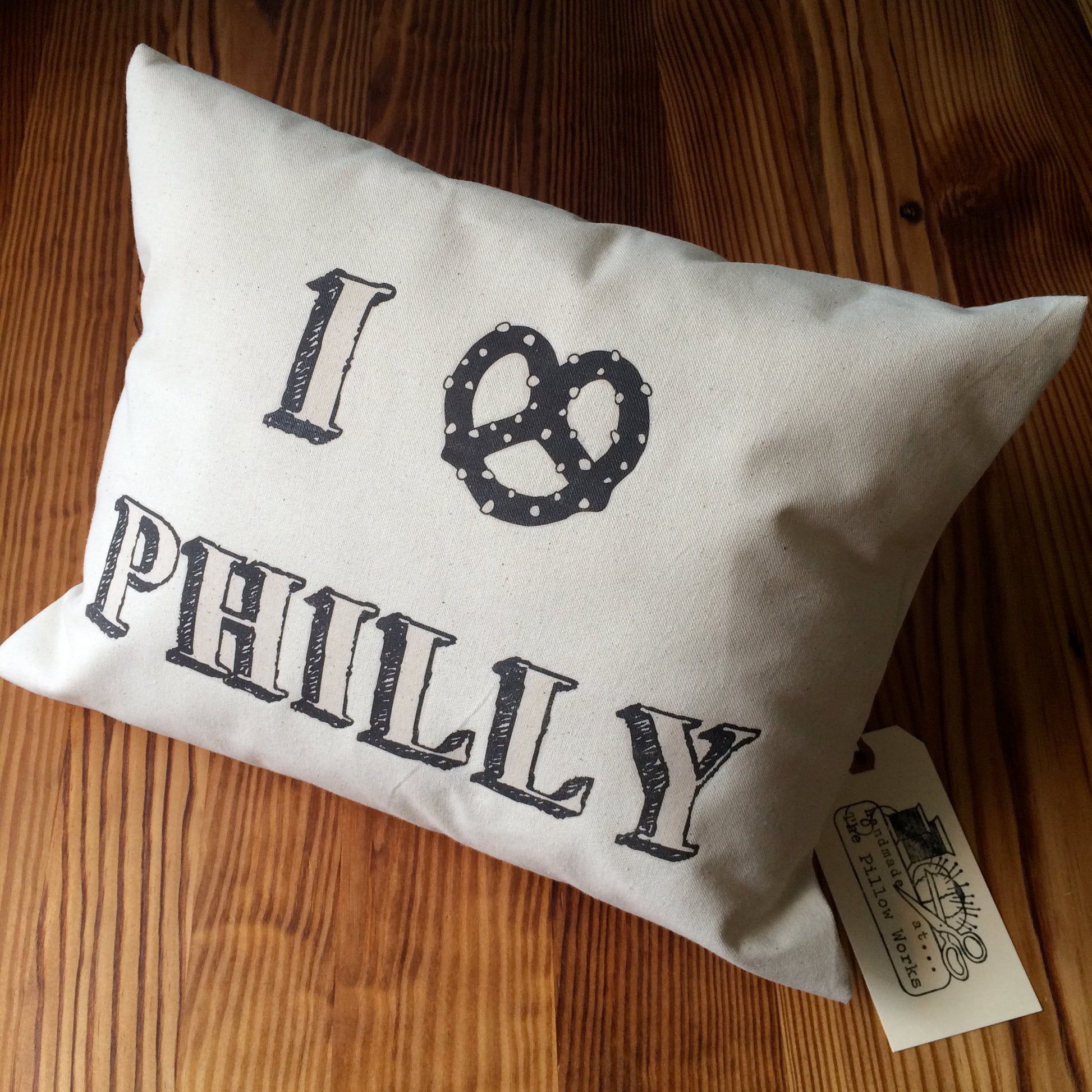 Decorative I Pretzel Philly Pillow by The Pillow Works, printed in black on an unbleached cotton drill fabric, displayed on a wooden surface.