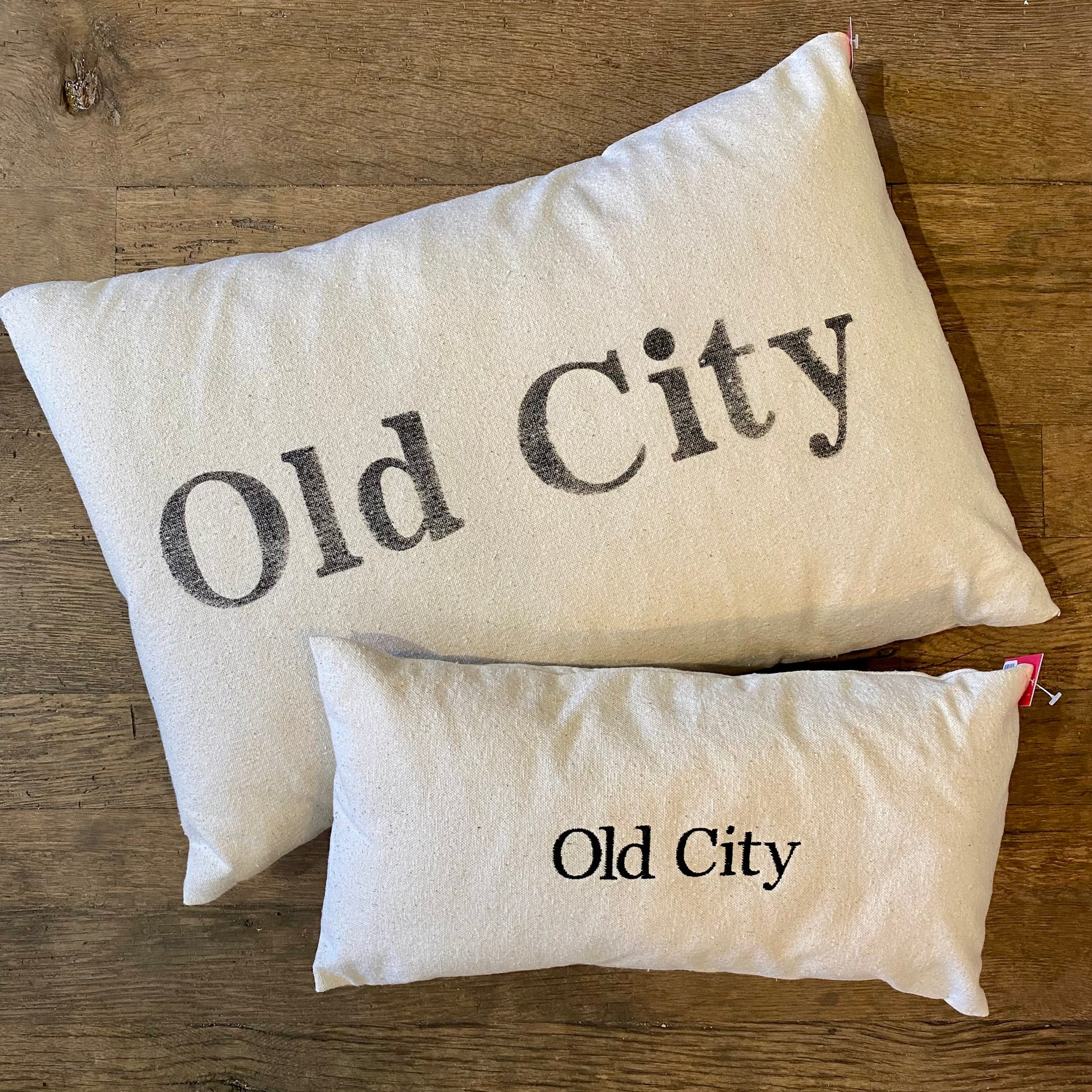 Two Old City Pillows with "Old City Philly" printed on them, one larger than the other, on a wooden floor by The Pillow Works.