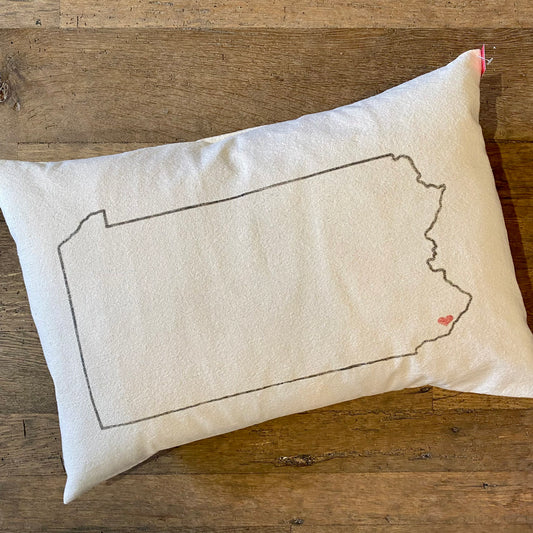 A Pennsylvania Heart Pillow from The Pillow Works, featuring a small red heart marking Philadelphia, embroidered on a rectangular pillow.