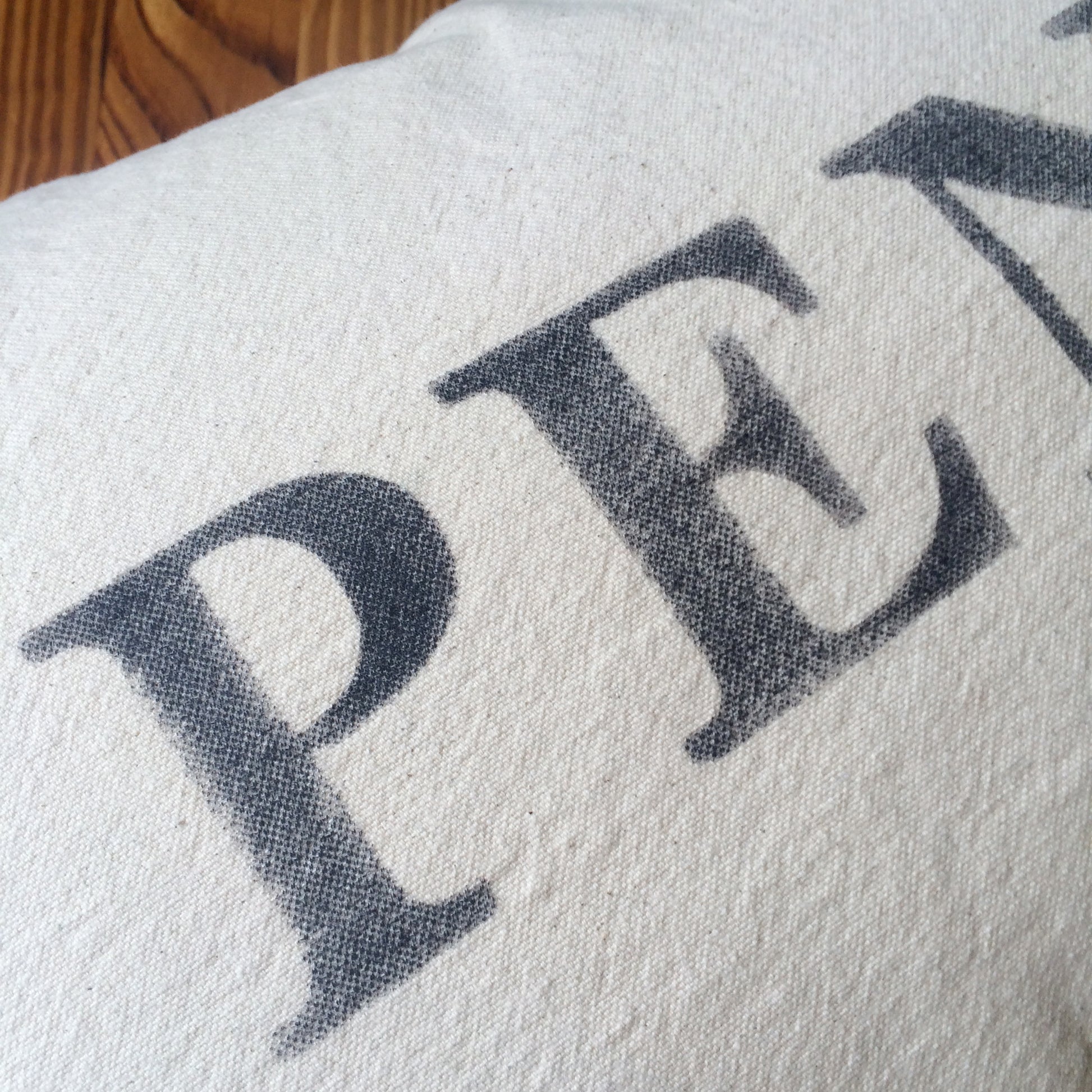 Close-up of a gray fabric with the black letters "P E R" printed in a serif font, part of University of Pennsylvania The Pillow Works school pride pillows.