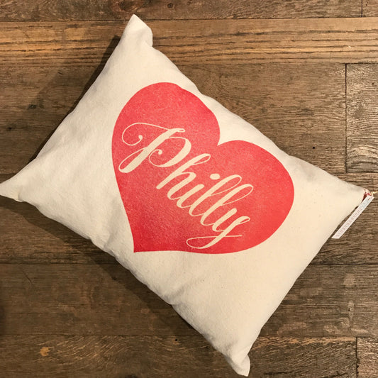 A Philly Heart Pillow by The Pillow Works with a red heart design and the word "philly" on a wooden floor, made from unbleached cotton drill fabric.