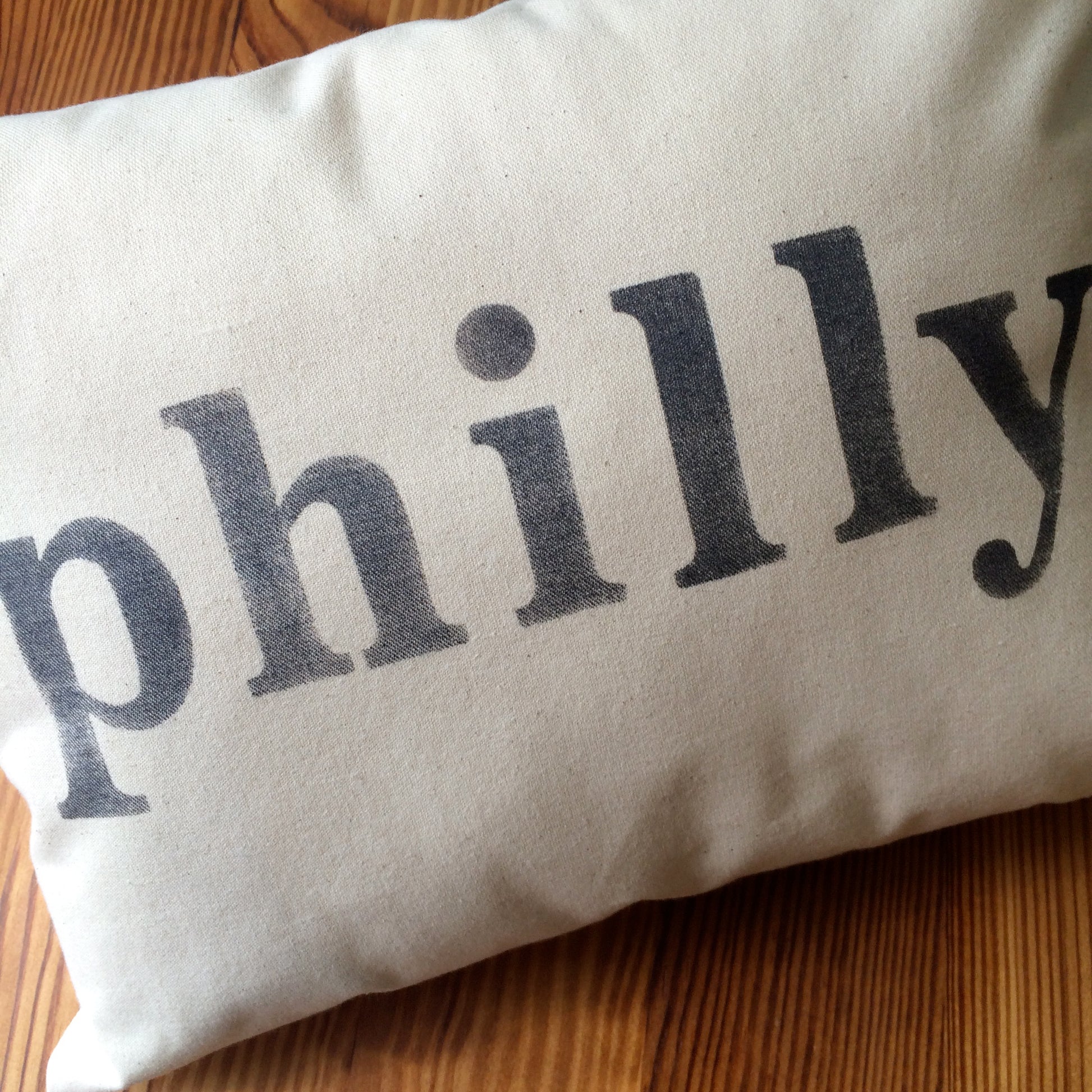 A close-up image of a beige Philly Pillow made of unbleached cotton with the word "philly" printed in bold black letters.