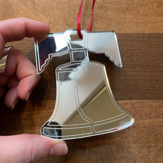 A hand holding a Philly-themed Liberty Bell Laser Cut ornament crafted from silver with a reflective surface by Rosewood Home.