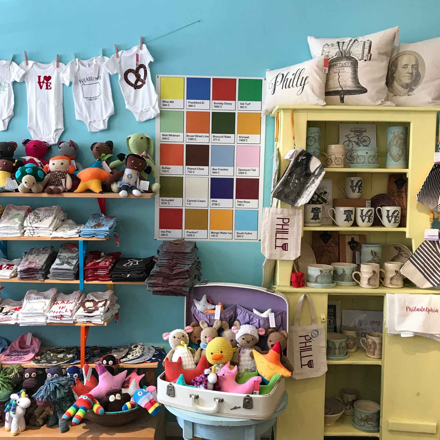 A gift shop display featuring souvenirs from Philadelphia, including South Fellini Philly Palette Poster, Tastykake Butterscotch Krimpets, t-shirts, stuffed toys, mugs, and various knick-knacks.