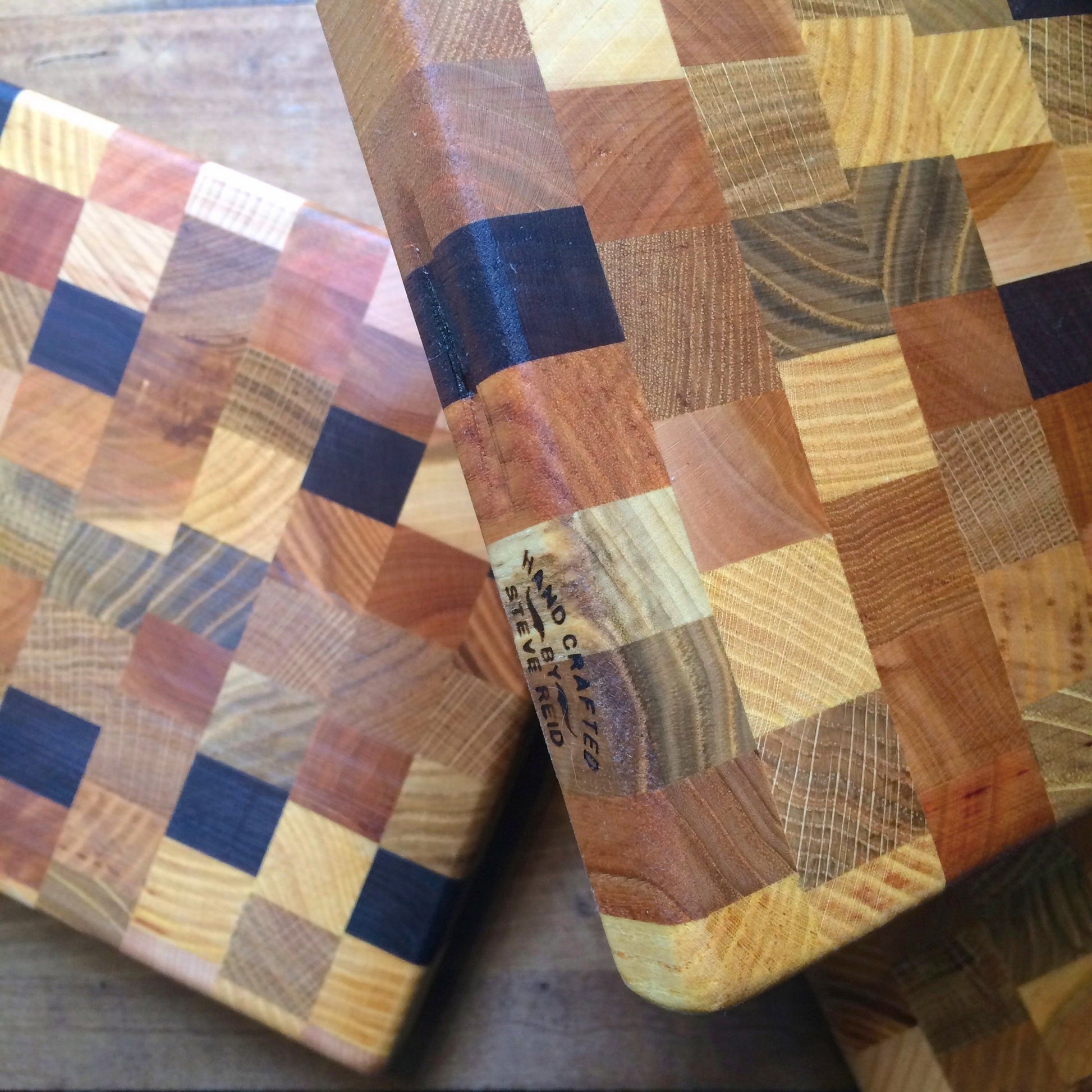 Close-up of two Steve Reid checkerboard wooden cutting boards with various shades, showing detailed wood grain patterns.