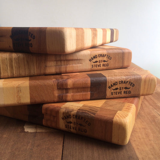 Four stacked Steve Reid Checkerboard Wood Cutting Boards with engraved text 