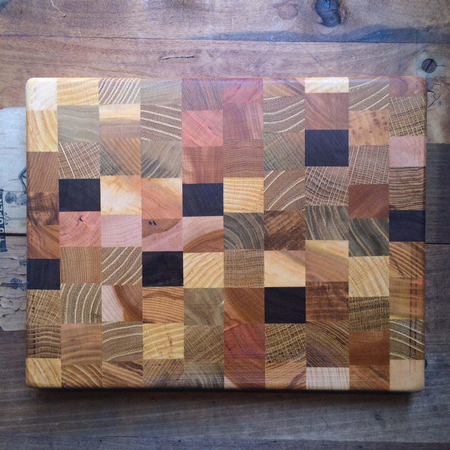 A Steve Reid wooden presentation board featuring a Checkerboard Wood Cutting Board design of various wood types laid out in a geometric pattern.