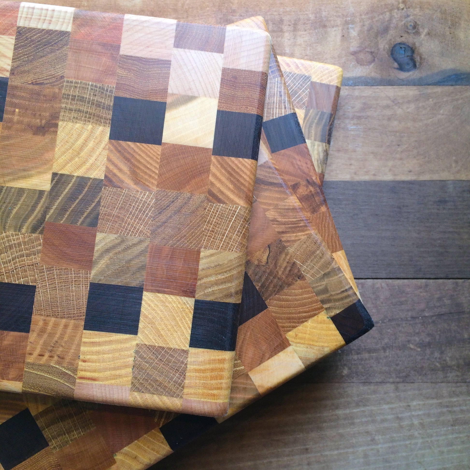 A multicolored end grain Steve Reid Checkerboard Wood Cutting Board displayed on a wooden table.