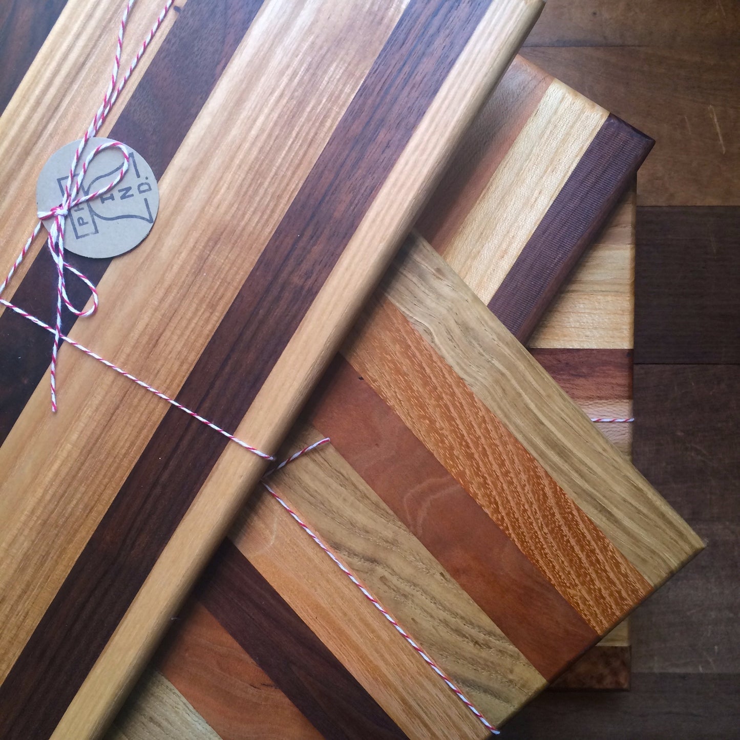 A collection of Steve Reid's Striped Wood Cutting Boards with varying wood grains and colors, tied together with twine and a tag.