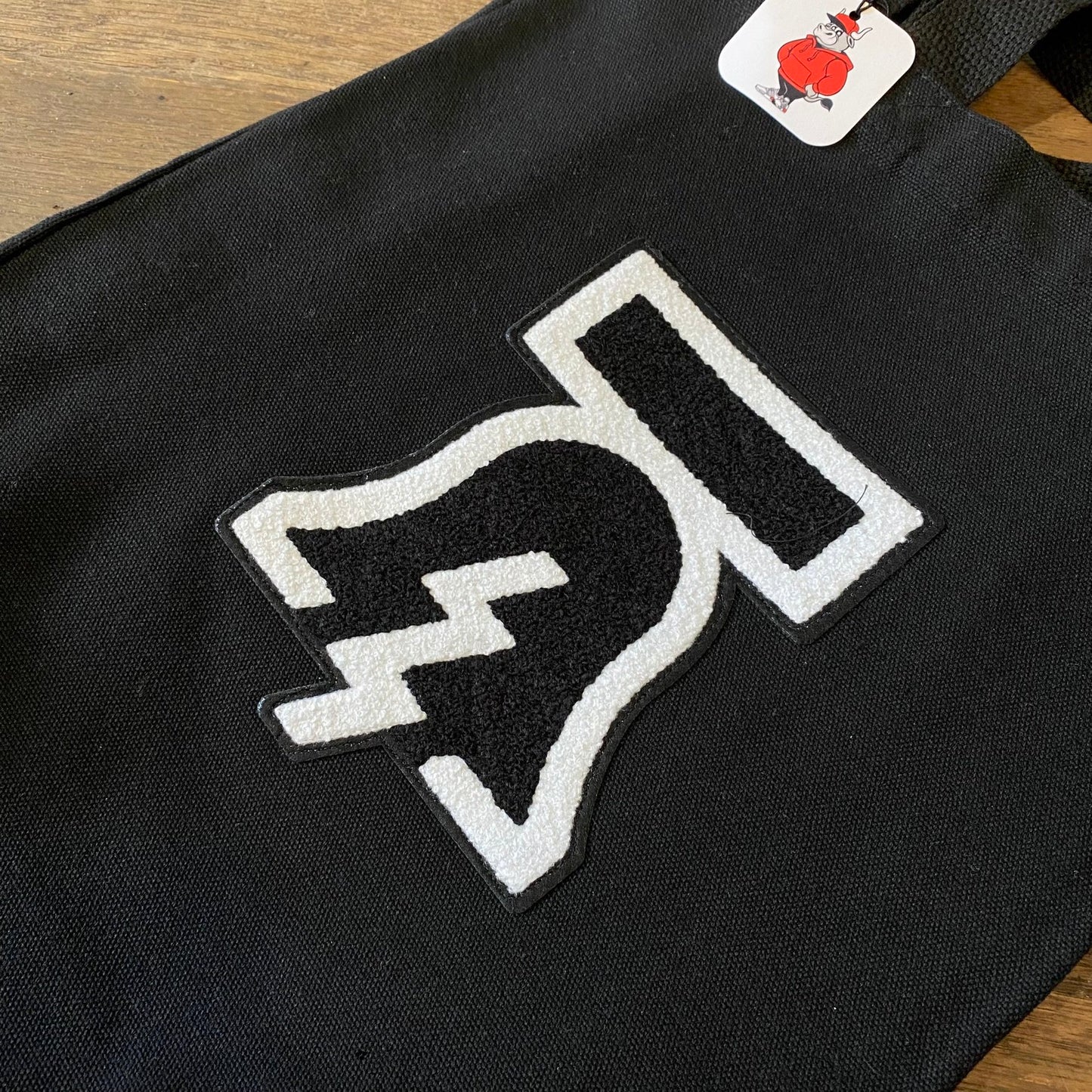 Bell & Bolt Patch Tote Bag with a white and black thumbs-down patch and a tag with a red character by Tote Jawn.