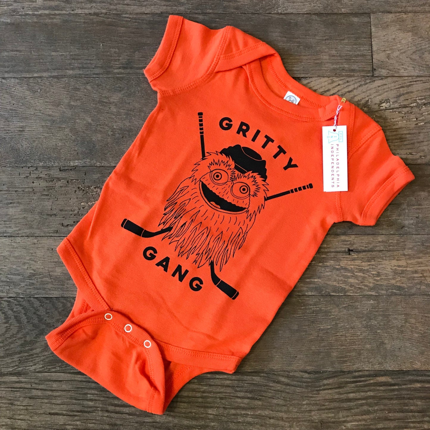 Orange Gritty Gang baby onesie by exit343design featuring the Philadelphia Flyers GRITTY cartoon character on a wooden floor.