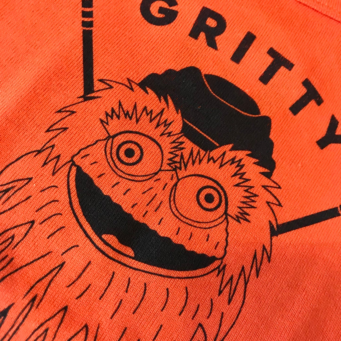 A close-up of an orange, 100% cotton fabric featuring an illustration of the Gritty Gang Baby Onesie by exit343design, the mascot for the Philadelphia Flyers hockey team.