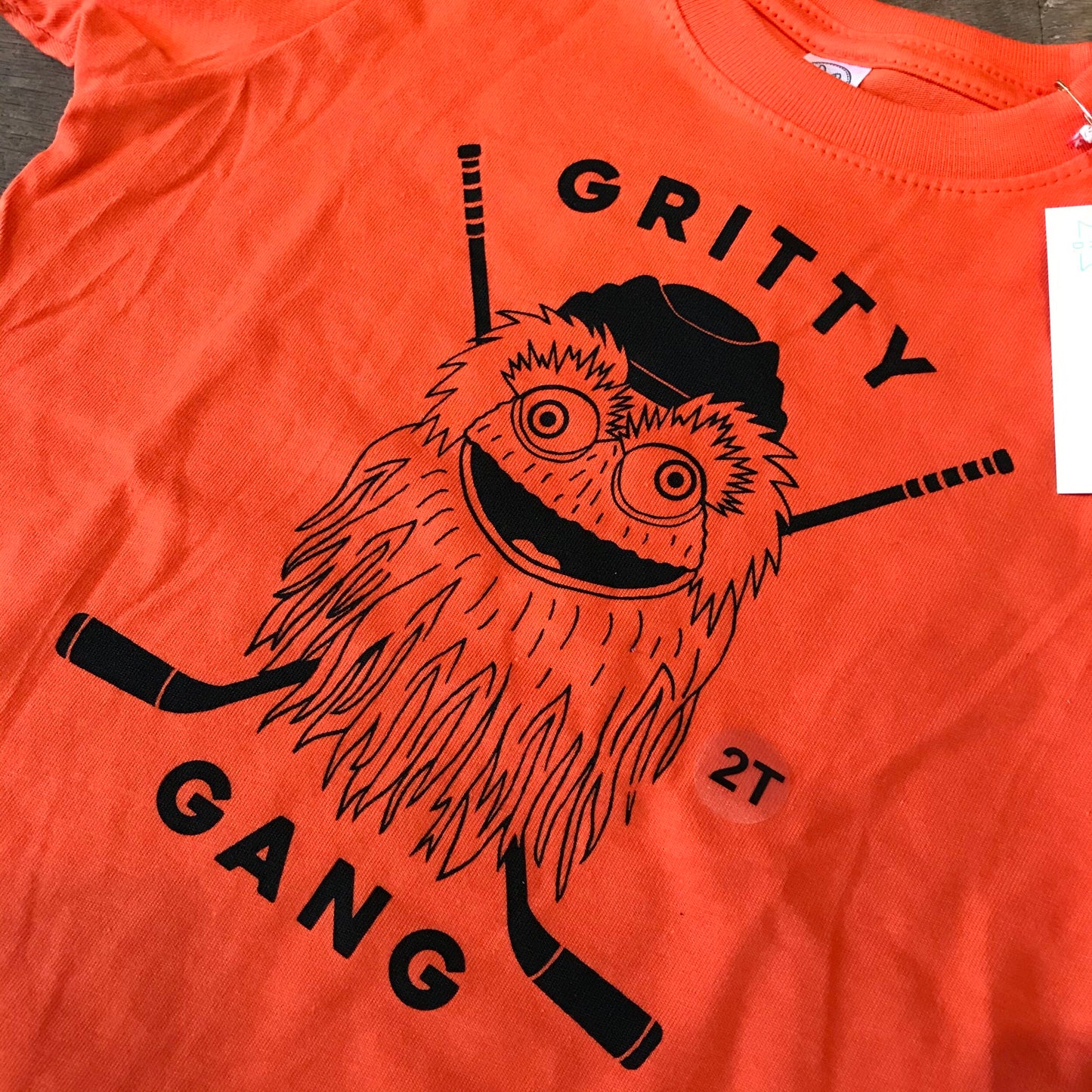 Orange Gritty Gang Toddler T-shirt by exit343design with a black graphic of a mascot-like figure holding hockey sticks and the words "gritty gang" printed on it.