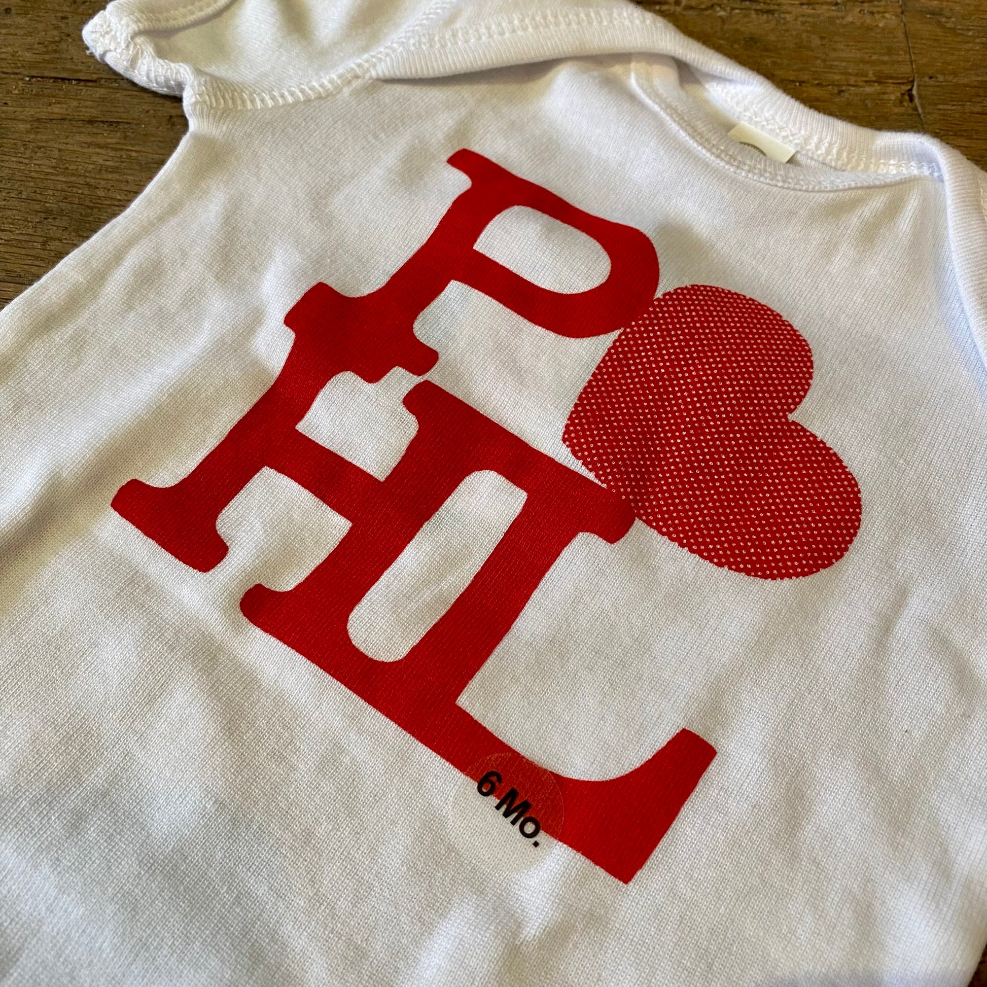 White cotton exit343design PHL Love Baby Onesie with a red "Philly love" sign and heart symbol on a wooden surface.