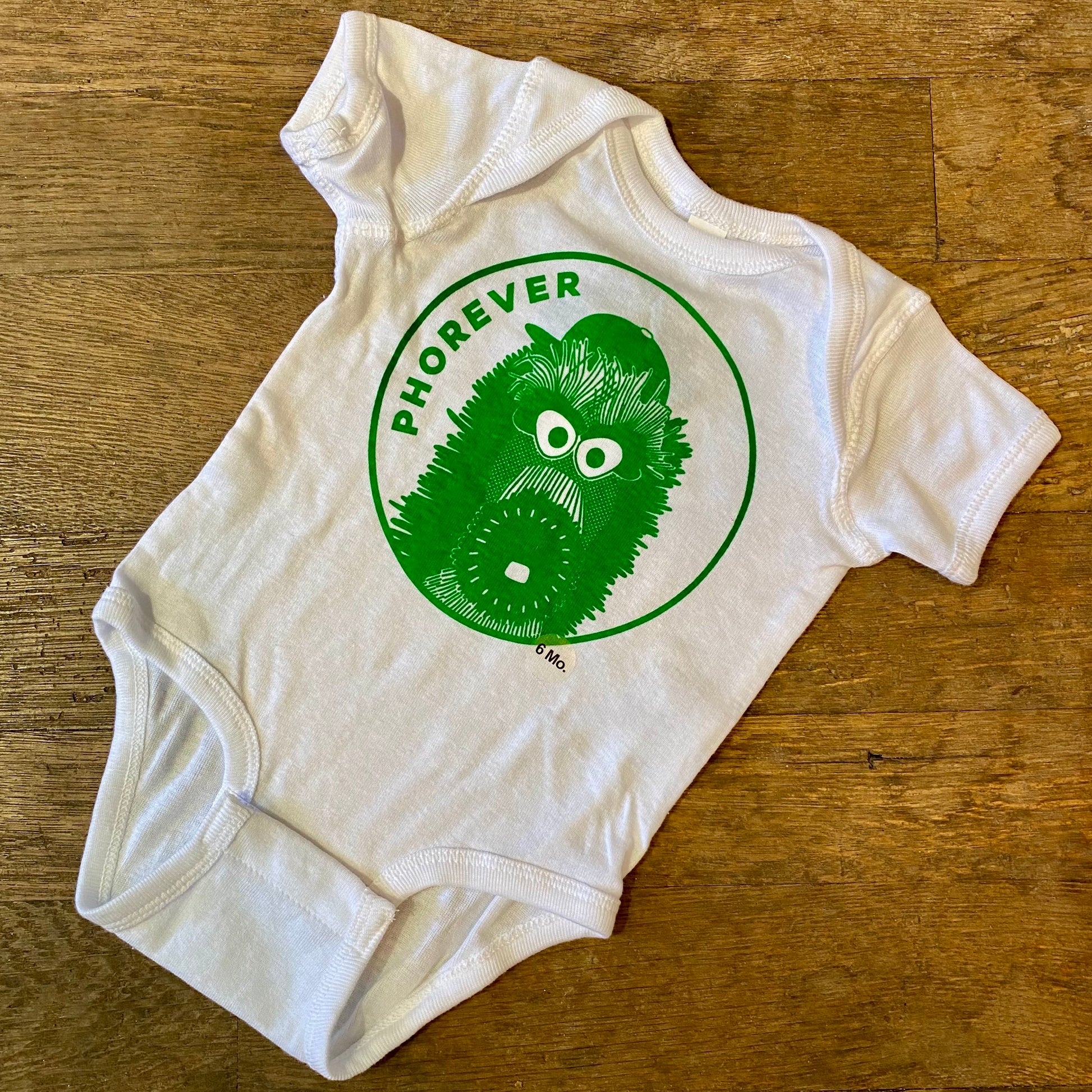 White Phanatic Phorever baby onesie with green "Phorever Phan" kiwi design on a wooden background designed by exit343design.