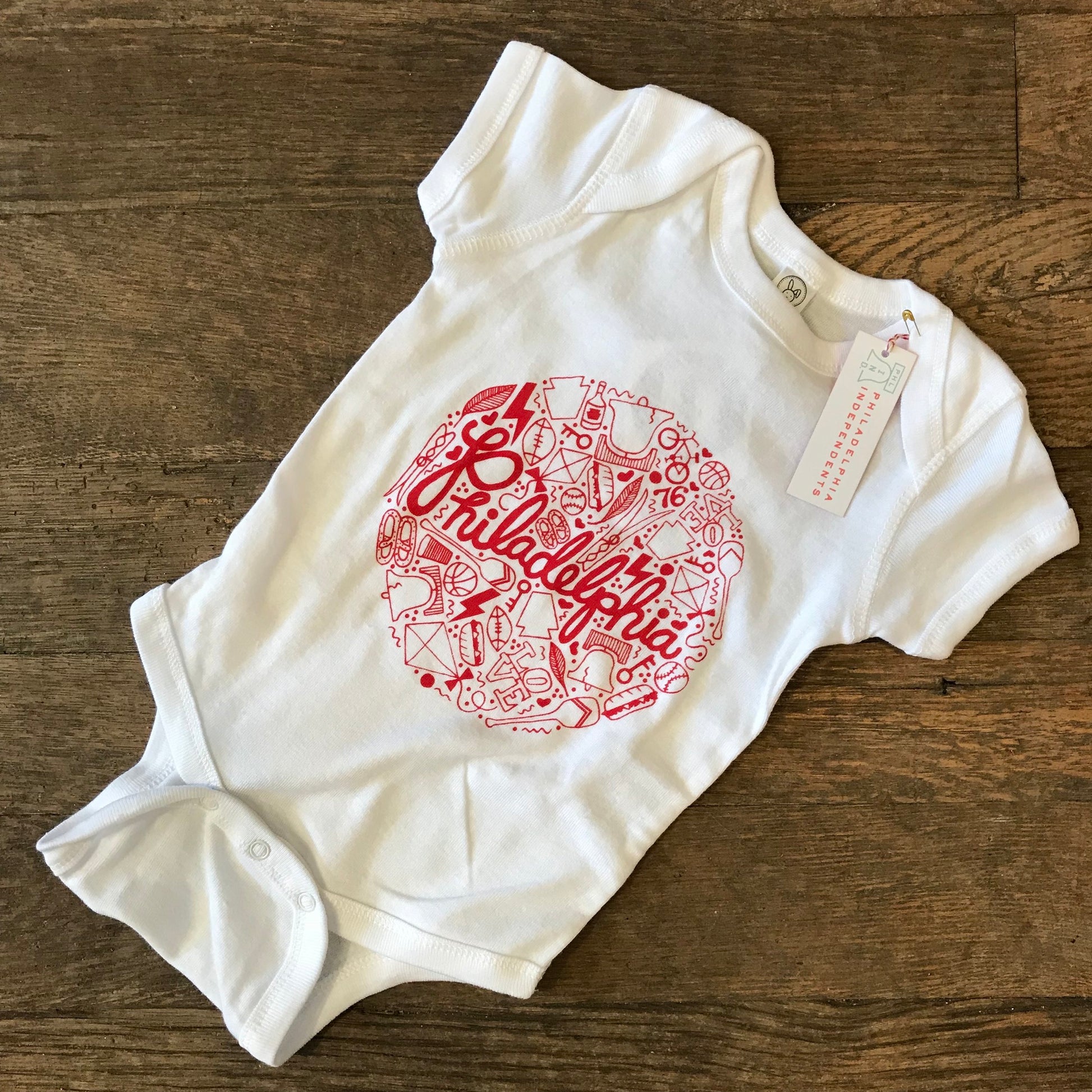 Sentence with replaced product:
Philadelphia Baby Onesie from exit343design with a red graphic print representing the Liberty Bell in Philadelphia, displayed on a wooden surface.
