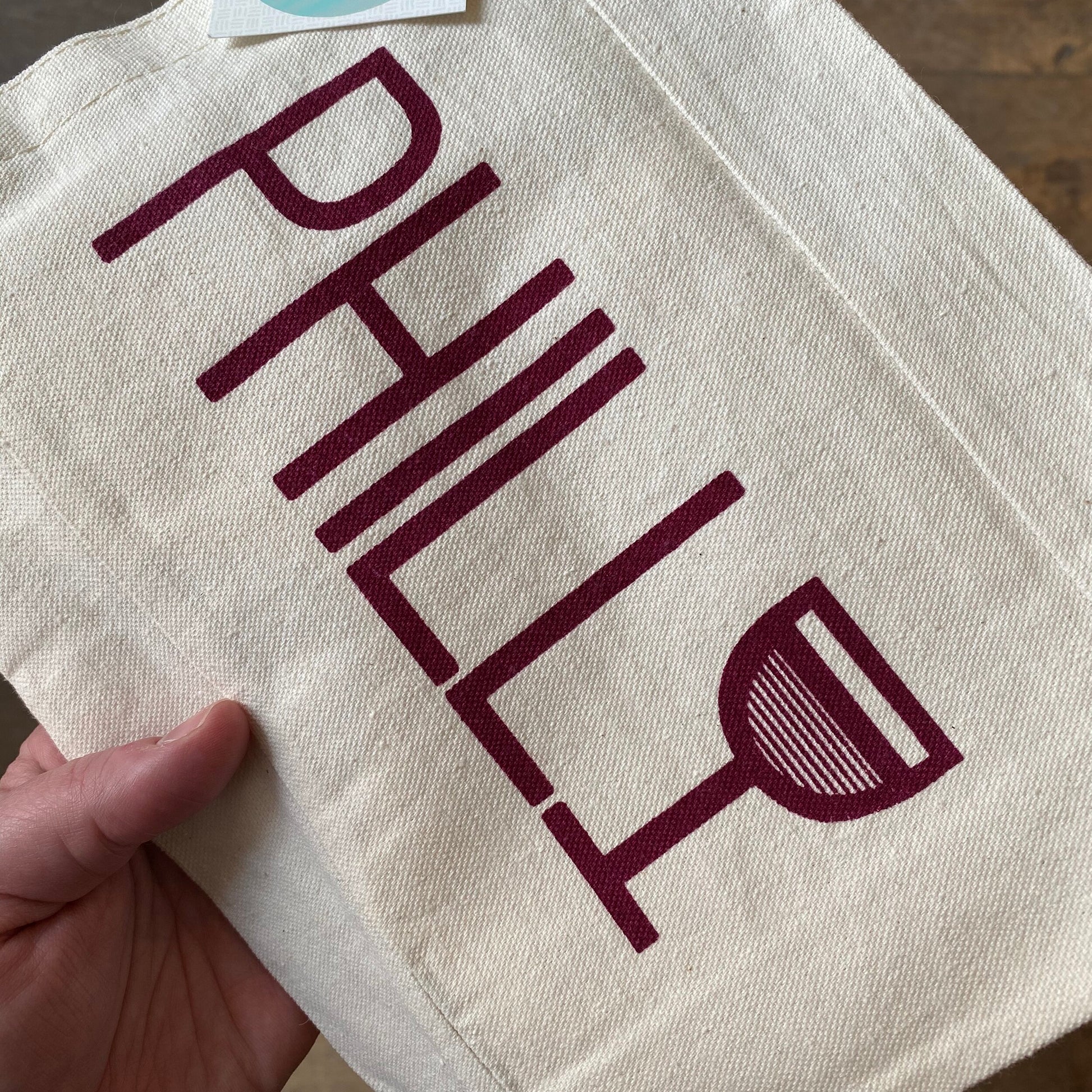 A hand-screenprinted canvas tote bag with the word "Philly" printed on it along with an illustration of a wine glass, called the "Philly Wine Tote" by exit343design.