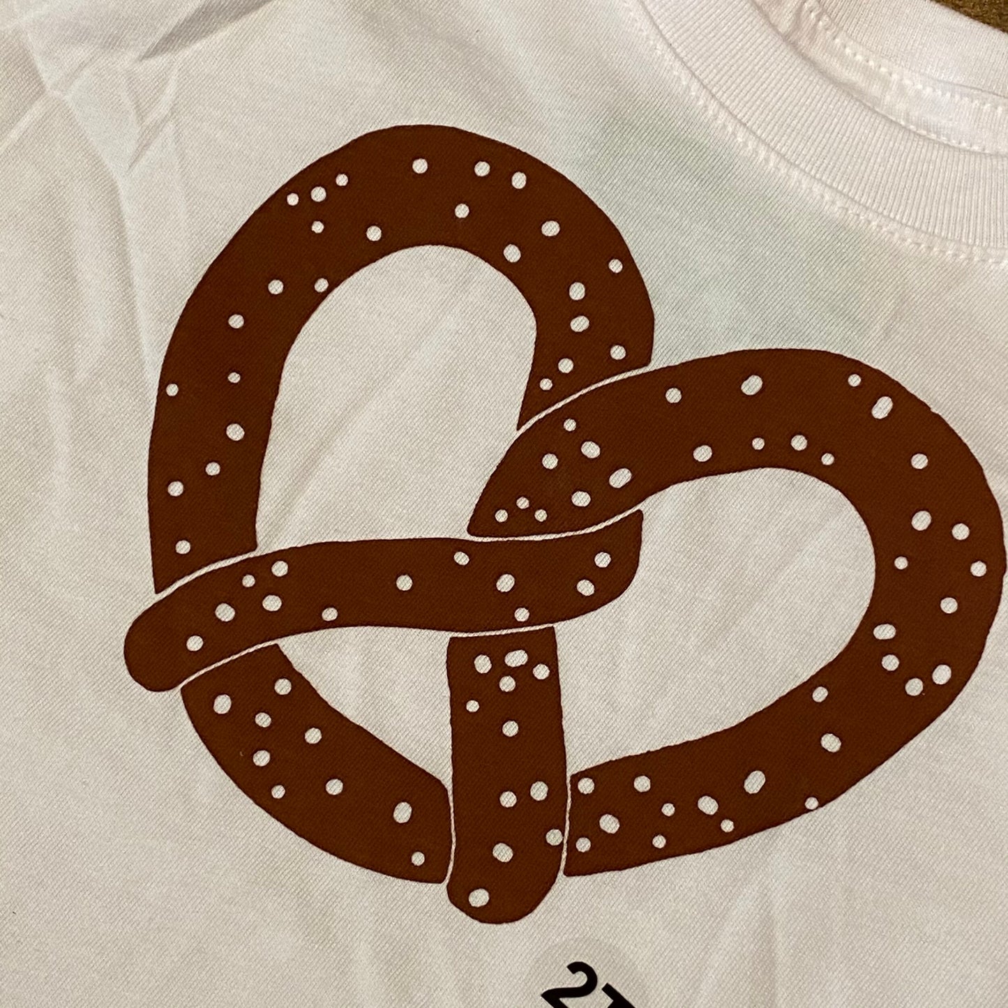 A graphic print of a brown Philly pretzel with white dots on a 100% cotton exit343design Toddler T-Shirt.